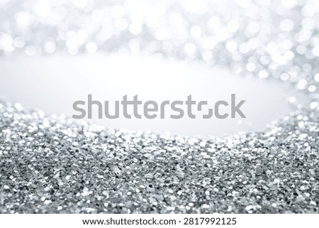 A close-up, shallow depth of field view of shimmering silver glitter, creating a festive and celebratory atmosphere with soft, out-of-focus bokeh lights in the background.