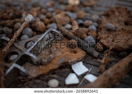 A close-up, shallow depth-of-field image of various rusty metal objects, corroded bolts, iron fragments, and weathered debris scattered on a textured surface.