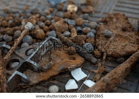 A close-up, shallow depth-of-field image of various rusty metal objects, corroded bolts, iron fragments, and weathered debris scattered on a textured surface.