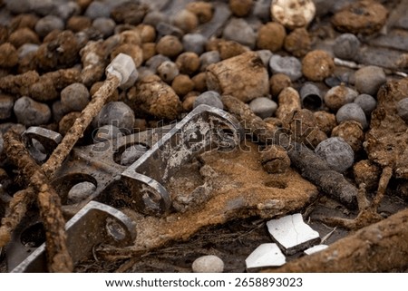 A close-up, shallow depth-of-field image of various rusty metal objects, corroded bolts, iron fragments, and weathered debris scattered on a textured surface.