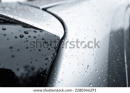 Close-up, shallow focus of fresh water droplets seen on the metallic paintwork of a hybrid, city car. Showing part of the rear black roof spoiler.