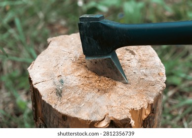 Close-up of a sharp black axe blade stuck in a wooden chopping log at an outdoor campsite