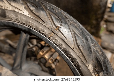 Close-up of a sharp rusty nail stuck in a motorcycle tire tread, illustrating vehicle breakdown, road hazard, and tire repair needs.