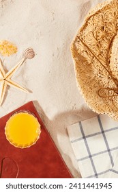 Close-up of shells, starfish, straw hat, notebook and a glass of orange juice on white sand. Summer scene with tropics. Scene for seasonal product advertising.