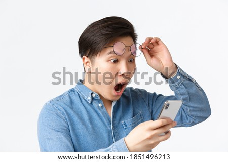 Close-up of shocked asian man take-off glasses, gasping in awe while looking at mobile phone screen, reading shocking news, react to announcement on smartphone, white background Stockfoto © 