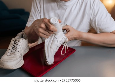 Closeup of shoemaker using bottle of shoe whitener and painting scuffed surface of dirty white sneaker, illustrating process of cleaning, recoloring, and restoring footwear.