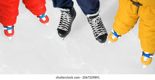 Close-up Of The Shoes Of Dad And  Kids Skating On Ice Rink. Banner With Copy Space For Skating Lessons And Training. Two Children In Orange And Red Overalls Next To A Hockey Coach. Young Athletes