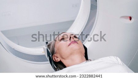 Close-up shoot of woman lying at moving scanner bed. Portrait of female waiting for magnetic resonance procedure. Patient dressed up in white undergoes MRI. Woman is entering in CT scanner.