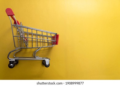 Close-up of shopping trolley (basket) on yellow background with some copy space.