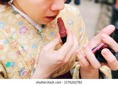 A Close-up Short Of An Anonymous Woman, In Flowery Yellow Japanese Traditional Costume Called Kimono, Puts On Red Lipstick While Looking In The Small Mirror