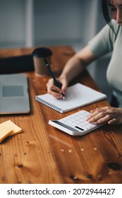 Close-up Shot Of Accountant Using Calculator While Taking Notes On Office Desk.