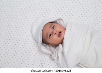 Closeup Shot Of An Adorable Baby Girl Wrapped With White Towel After Shower. A Southeast Asian Baby In White Blanket On White Background Cloth. Top View.