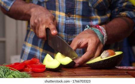 A closeup shot of an African-American man's hands cutting an avocado with a big sharp knife - Powered by Shutterstock