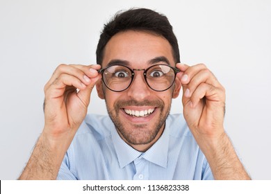 Closeup shot of amazed young European handsome male, looking through round spectacles, touches rim of glasses, smiling with healthy toothy smile posing in studio. People, emotion and lifestyle concept