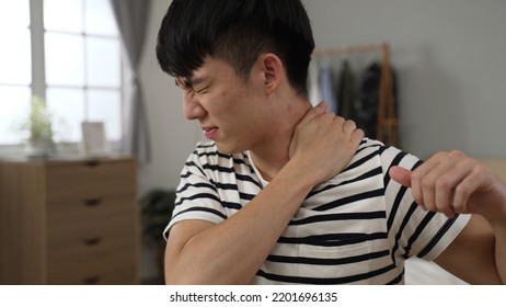 closeup shot asian Chinese male suffering shoulder stiffness is having a massage with a grimacing face while learning from home in the bedroom - Shutterstock ID 2201696135