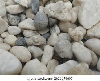 Close-up shot of assorted smooth river pebbles and stones in white, gray, beige, and off-white tones. Natural textures, varied shapes and sizes, earthy neutral color palette, organic rocky background.