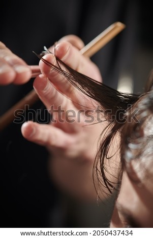 Close-up shot of a barber's hands making a haircut. Handsome brunet man visiting a hairstylist in a barbershop.