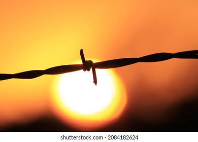 A closeup shot of a barbwire fence at Sunset with the sun and a colorful sky north of Hutchinson Kansas USA out in the country.