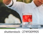A close-up shot of a bartender preparing a refreshing red drink with ice cubes in a decorative glass, perfect for summer events