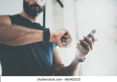 Close-up Shot Bearded Sportive Man After Workout Session Checks Fitness Results Smartphone.Adult Guy Wearing Sport Tracker Wristband Arm.Training hard inside gym.Horizontal bar background.Blurred - Powered by Shutterstock