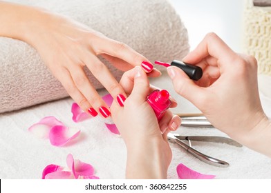 Closeup shot of a beautician applying nail polish to female nail in a nail salon. Close up of a woman hand with pink nailpolish after the manicure. 