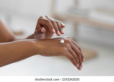 Closeup Shot Of Black Lady Applying Drop Of Moisturising Cream On Hands, Cropped Image Of Young African American Woman Using Nourishing Lotion For Dry Skin Treatment, Making Beauty Routine At Home