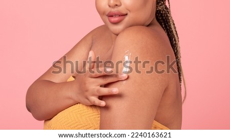 Closeup shot of black plus size lady rubbing moisturising lotion to skin on shoulder, woman applying nourishing cream, enjoying body care, pink background, panorama, cropped