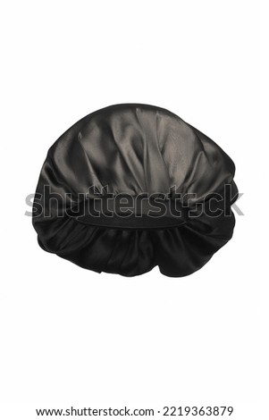 Close-up shot of a black sleep cap with a wide elastic band. A satin hair bonnet for protecting hair at night is isolated on a white background. Front view.