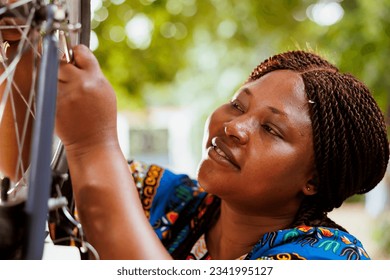 Close-up shot of black woman gripping spanner for tightening bicycle parts outdoor. Detailed image of female african american cyclist repairing bike wheel for secure leisure cycling. - Powered by Shutterstock