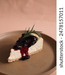 A close-up shot of a blueberry cheesecake slice, garnished with a fresh sprig of rosemary. 