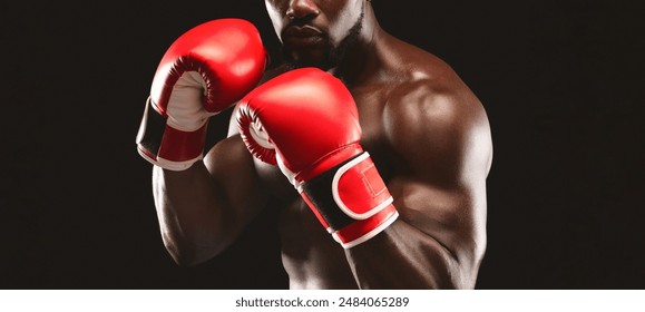 A close-up shot of a boxer wearing red boxing gloves against a black background. The boxer is looking directly at the camera with a determined expression. - Powered by Shutterstock