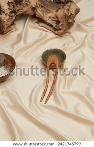 Close-up shot of a brown wooden hair pin in oriental style. A natural wood hair fork lies on a beige background near a bowls. Top view.
