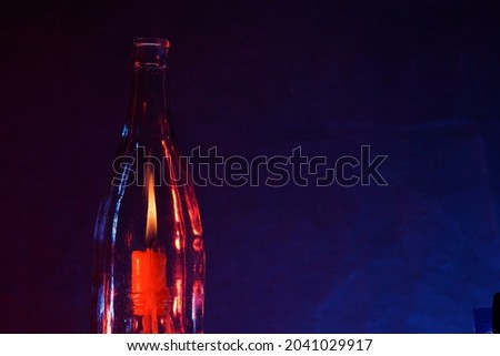 A closeup shot of a burning candle behind an empty glassy bottle in front of a dark blue background