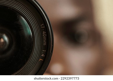 A close-up shot of a camera lens with a 17-40mm focal length. In the background, a young black man's head can be seen slightly out of focus