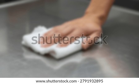 A close-up shot captures a hand using a white cloth to wipe down a stainless steel surface, emphasizing cleanliness and hygiene.