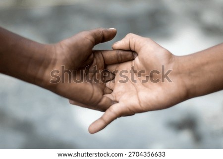 A close-up shot captures two hands, one darker and one lighter, firmly clasped together, symbolizing unity, support, and the bridging of differences.