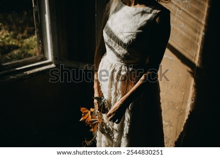 A close-up shot capturing the delicate hands of a woman gently holding autumn leaves against a textured white dress. The warm sunlight highlights the soft details, creating an intimate, poetic mood