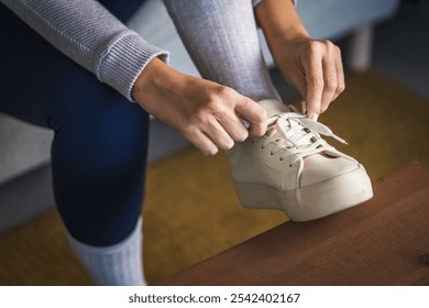 A close-up shot capturing hands tying the laces of a white sneaker resting on a wooden surface, showcasing a moment of preparation and everyday routine.