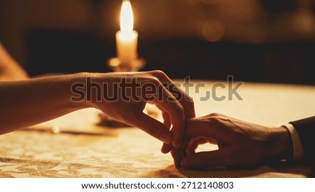 A close-up shot capturing a tender interaction between two people, where their fingers are delicately touching across a table illuminated by the soft glow of a single lit candle, suggesting a romantic