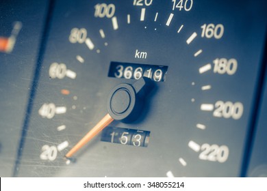 Close-up shot of car speedometer showing km/h, with orange pointer and white numbers over dark background. Tinted effect