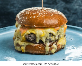 A close-up shot of a cheeseburger with melted cheese and sauce on a blue plate. The burger is topped with sesame seeds and a wooden stick is sticking out of the top. - Powered by Shutterstock