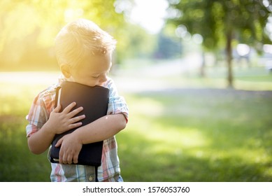 A Closeup Shot Of A Child Holding The Bible Against His Chest With A Blurred Background