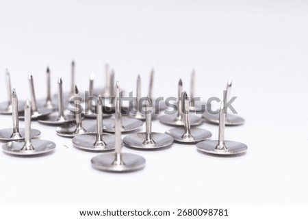 Close-up shot of a cluster of silver thumb tacks against a clean white background, showcasing office supplies and metallic pins.