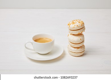closeup shot of coffee cup and stack of macaroons on white wooden table 