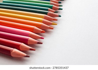 A close-up shot of a colorful array of sharpened colored pencils, arranged in a diagonal line, showcasing a gradient of hues from red to green against a clean white surface, perfect for art and creat.
