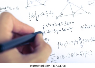 Closeup shot of complex math formulas on paper with hand holding ball pen aside.