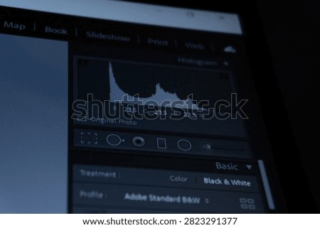 A close-up shot of a computer screen displaying photo editing software interface, focusing on the histogram display panel, color values, and basic adjustment controls in a dark environment.