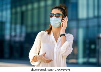 Close-up shot of confident woman wearing face mask and talking with somebody on her mobile phone while walking in front of business center during coronavirus pandemic. - Shutterstock ID 1709939395