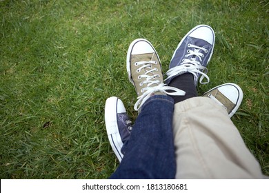 A Close-up Shot Of Couple Entwined Sneakers Over Grass.