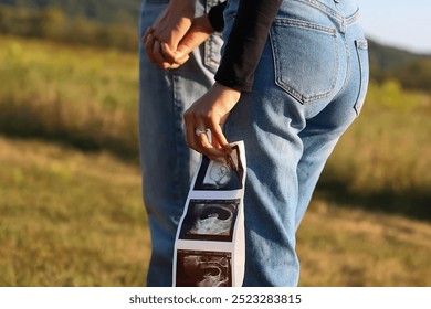 A close-up shot of a couple holding hands, with the wife displaying ultrasound images of their unborn baby. The photo highlights a special moment of their pregnancy announcement. - Powered by Shutterstock